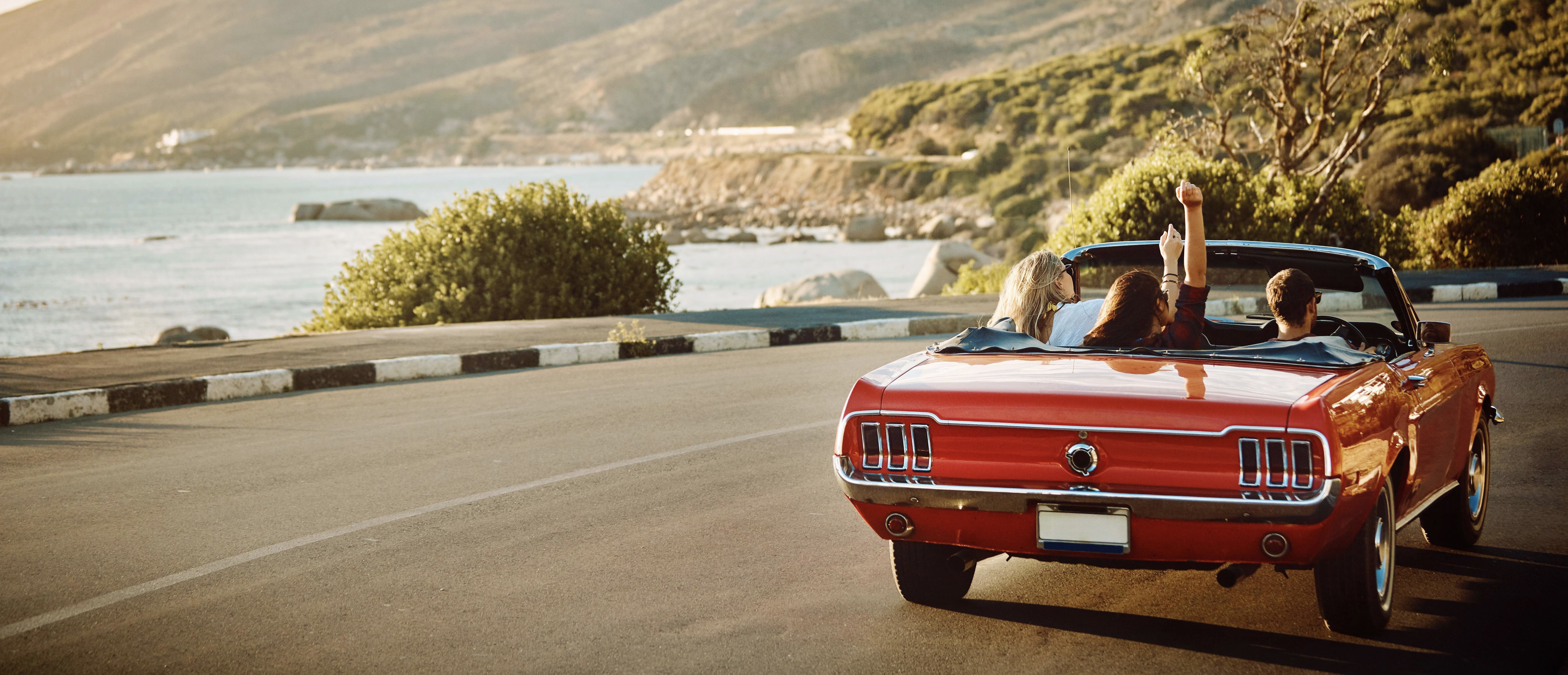 Friends enjoying a scenic driving experience along the coast in a classic rental car